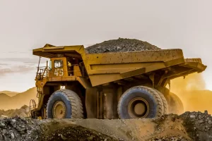 a large yellow dump truck on a mining site seen on the horizon of a sunset