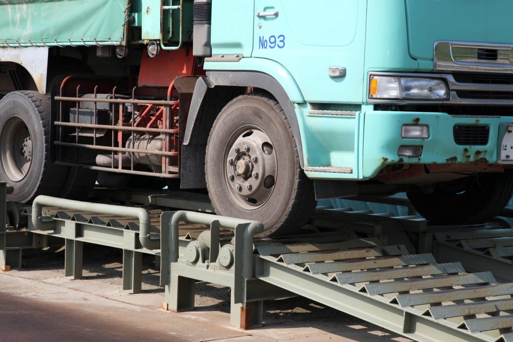 a turquoise truck at a close up right-front side angle driving over a weighbridge